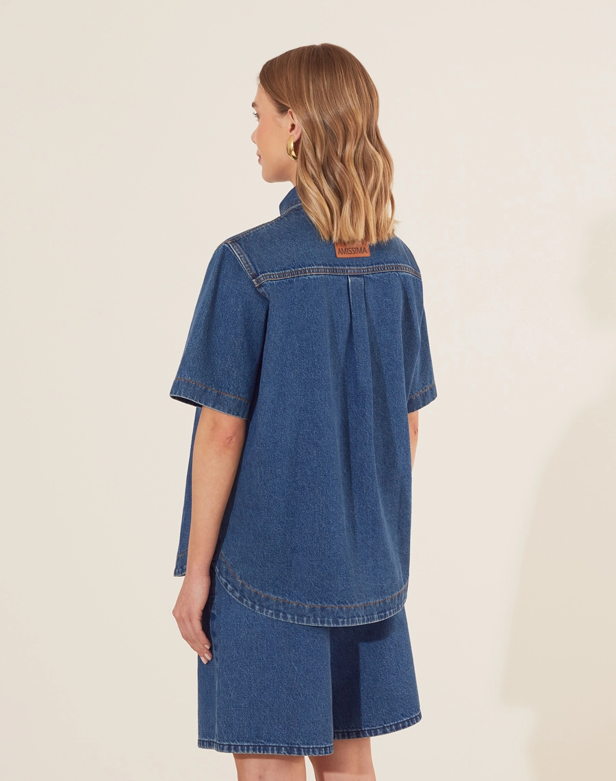 Camisa Bonnie confeccionada em jeans com lavagem escura. <br/>
Possui modelagem ampla e confortável, com mangas curtas e dois bolsos frontais que agregam praticidade. <br/>
O fechamento é frontal por botões de casa, trazendo um toque clássico e atemporal ao look. <br/>
Versátil, pode ser usada aberta como sobreposição ou fechada, compondo combinações modernas e despojadas.<br/>