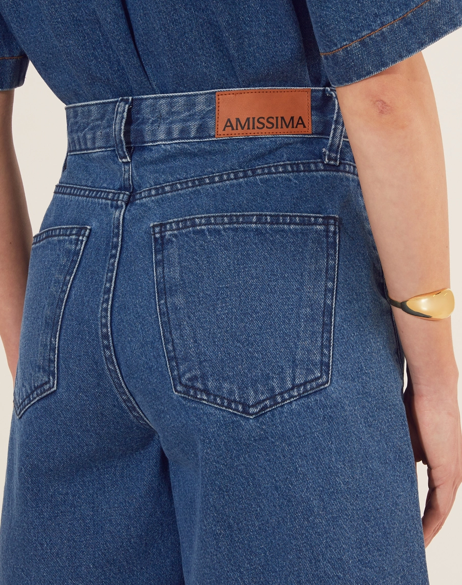 Bermuda confeccionada em jeans de lavagem escura com cintura alta.<br/>
 Apresenta uma modelagem solta e confortável, garantindo liberdade de movimento.<br/>
 Possui bolsos frontais funcionais e detalhes em costura contrastante que adicionam um toque moderno à peça. <br/>
Fechamento por zíper e botão de casa, tornando-se perfeita para compor looks casuais e elegantes.<br/>