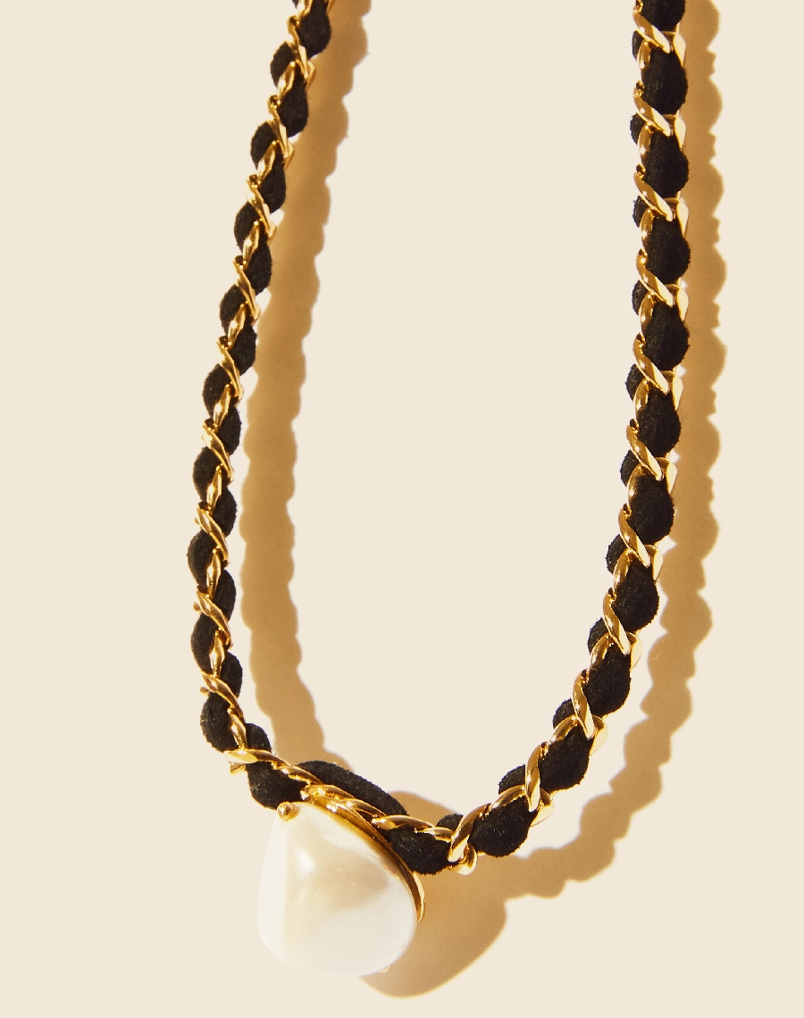 Colar Heart Chain confeccionado manualmente em corrente de elo grumet banhada a ouro com fio de couro e pingente frontal de pérola shell. <br/>
Possui fecho lagosta para regulagem.