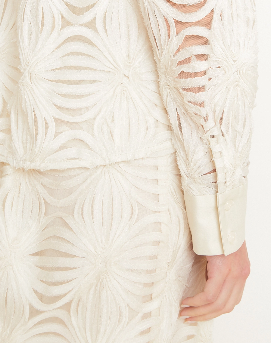 A Camisa Palmo é confeccionada em Tule bordado, um tecido leve e delicado, com transparência sutil e desenhos em relevo que enriquecem a peça com um visual sofisticado e feminino.